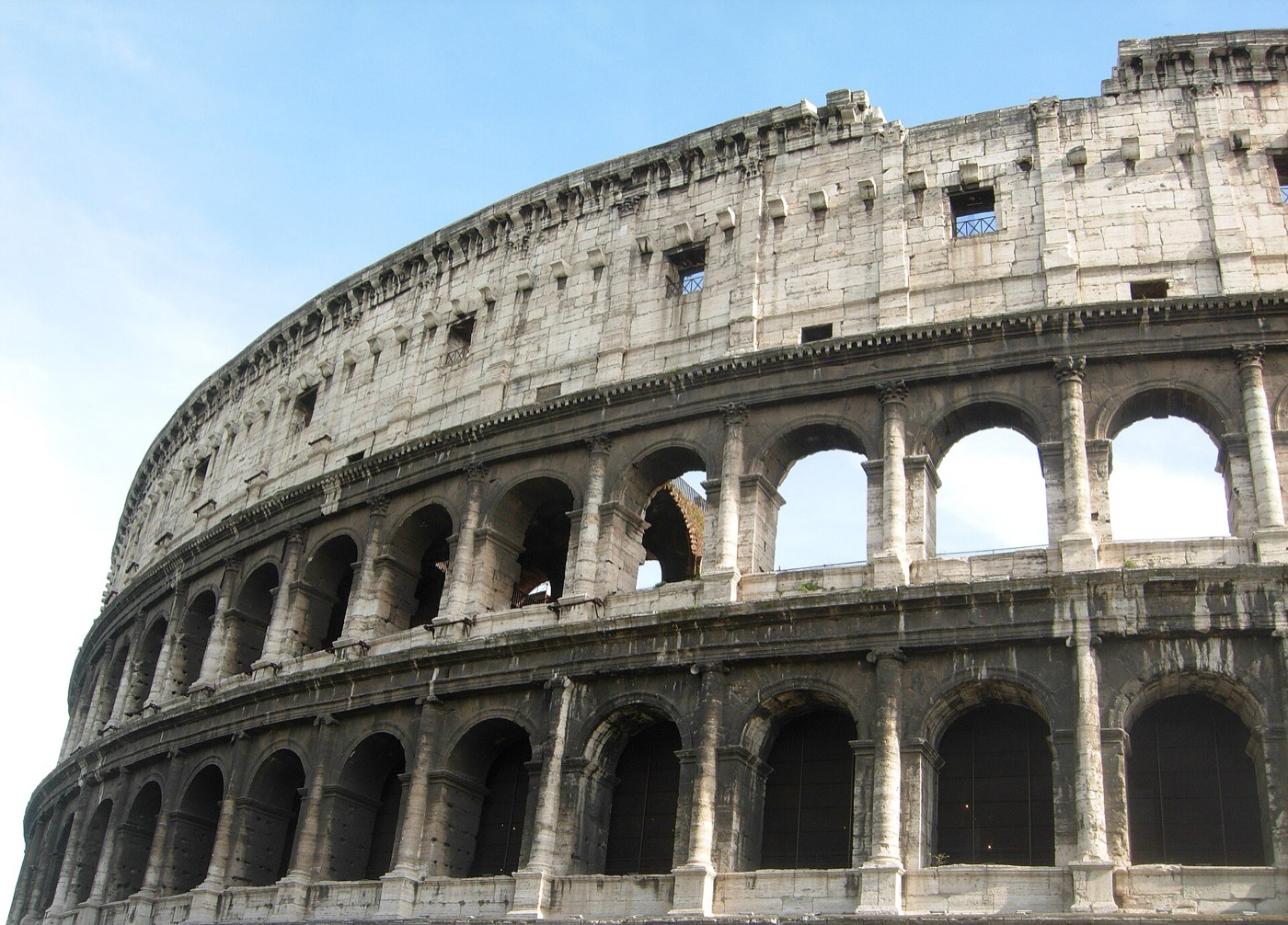 The outer wall of the Colosseum in Rome, three rows of arches against a pale sky