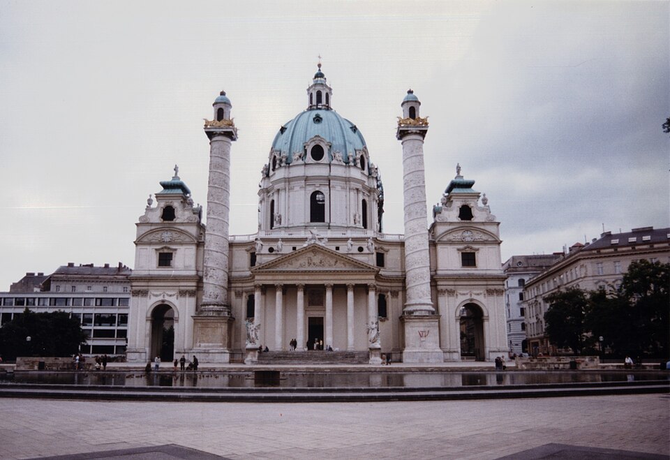 The Karlskirche in Vienna, a green dome between two carved columns, seen from the square